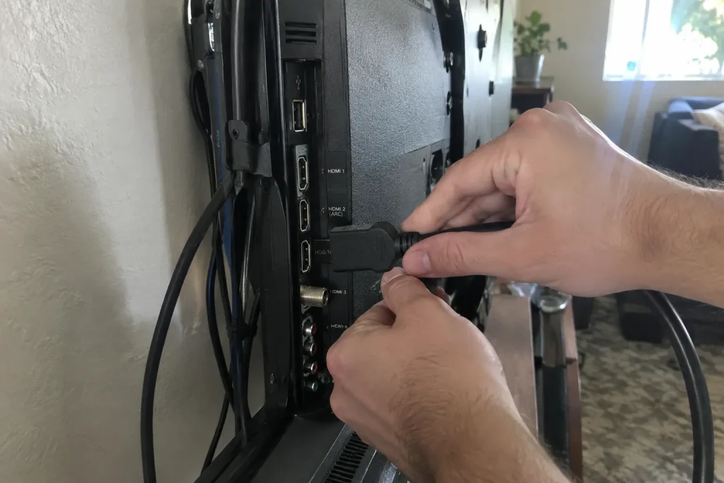 Ett par händer kopplar in en HDMI kabel i tv:ns baksida, del av Philips Hue Play HDMI Sync Box 4K test.